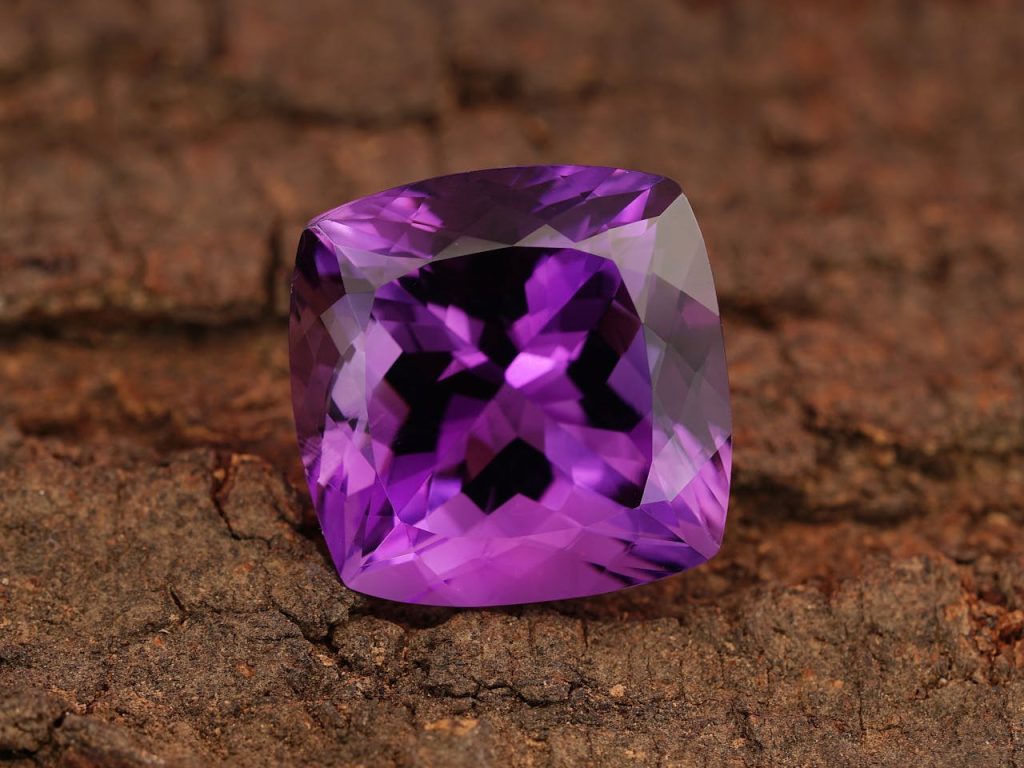 Close-up of a radiant purple amethyst gemstone on a textured wood surface.